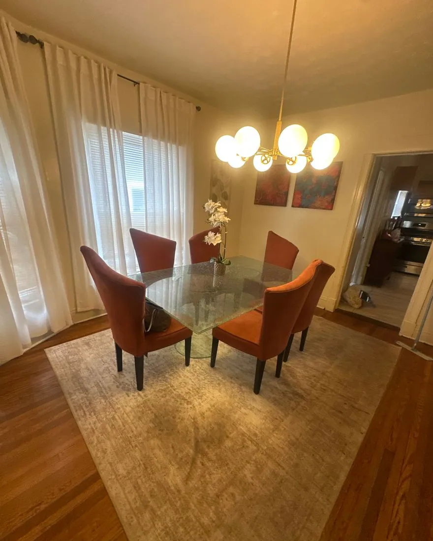 Dining room with a glass table, orange chairs and a globe chandelier after a Mama Meg clean