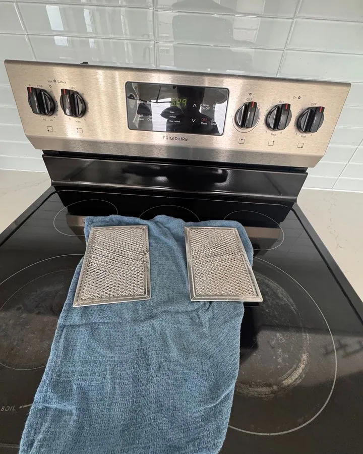 Range hood filters drying on a towel on a stovetop during a clean